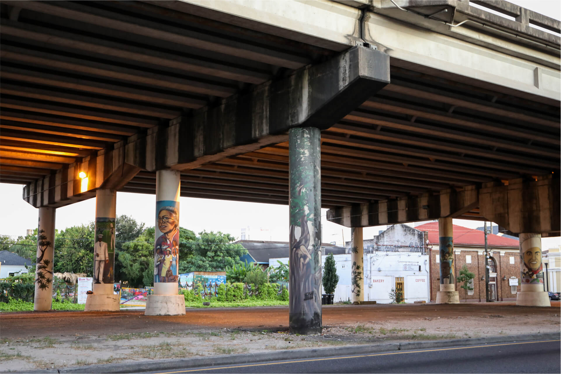 An overpass with murals on the support pillars and a decaying building on the other side of the street