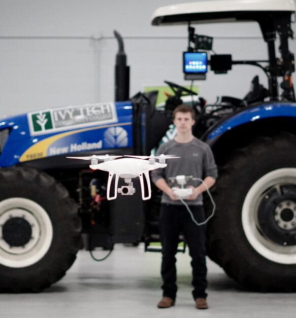 Student operates a drone while standing in front of a large tractor