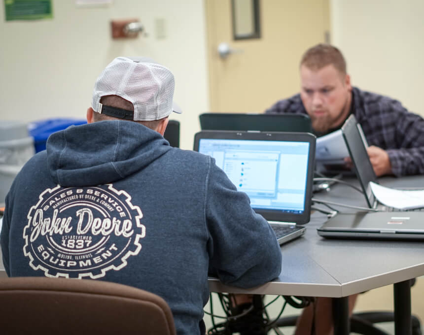 Ivy Tech students work on their laptops, one wearing a sweatshirt that says John Deere