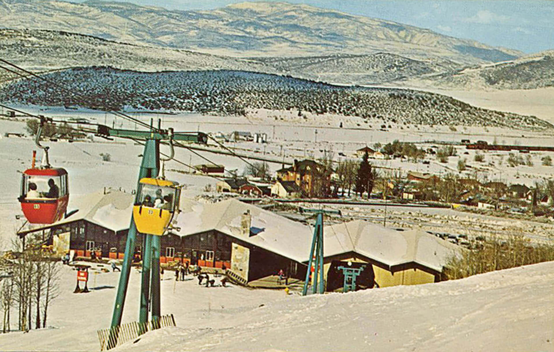 People riding the ski gondola in the foreground with the ski lodge behind in the distance