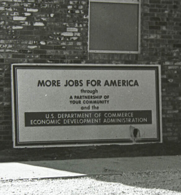 A sign on the side of a building that says "More Jobs for America through a partnership of your community and U.S. Department of Commerce Economic Development Administration"