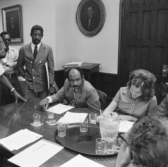 Herman J. Russell speaking at a meeting with many people gathered around a table